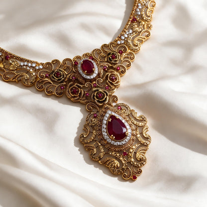 Close-up of the necklace floral centre and red teardrop pendant with clear decorative accents on ivory fabric.