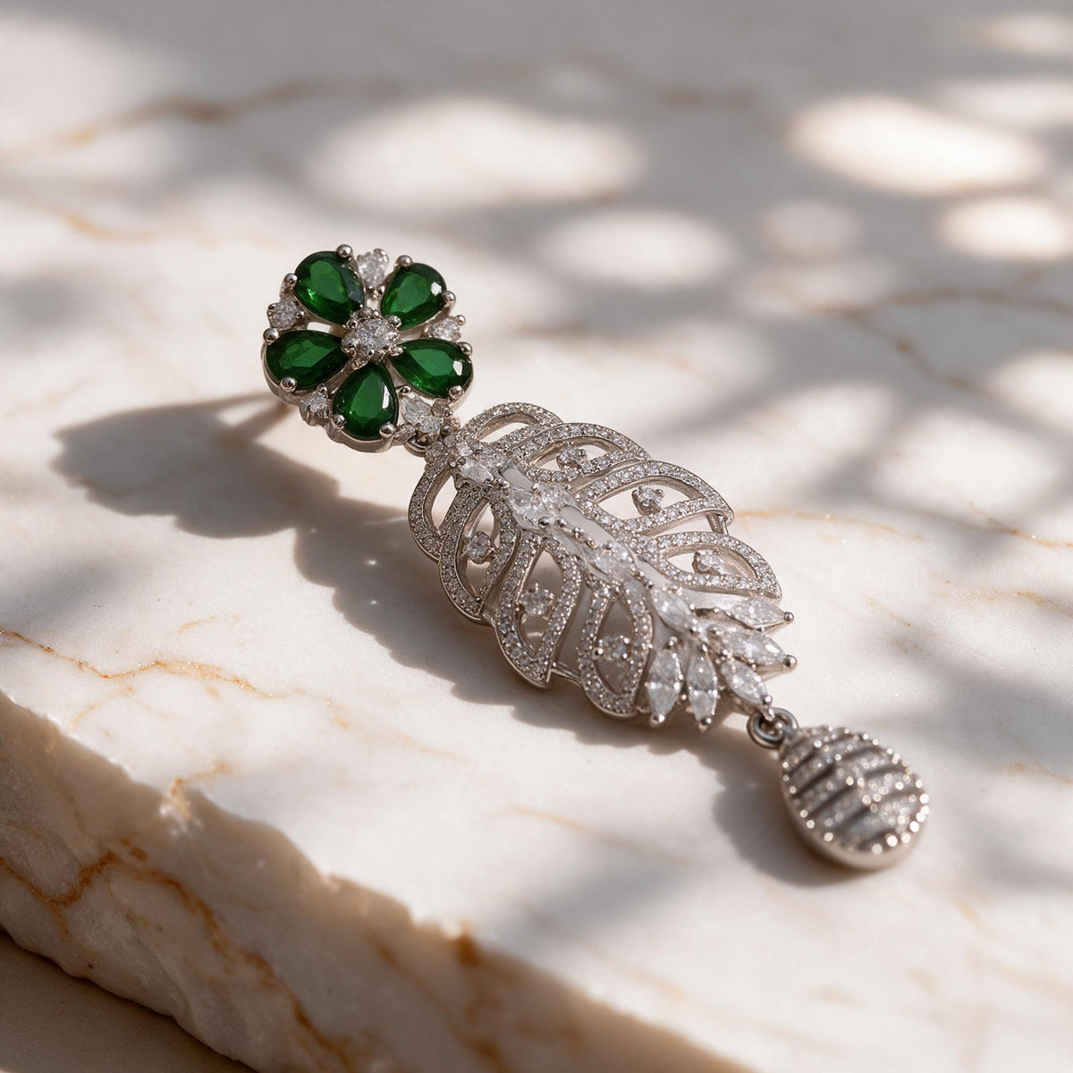 Close-up of a green floral earring top, open leaf-shaped drop and clear-accented teardrop pendant.