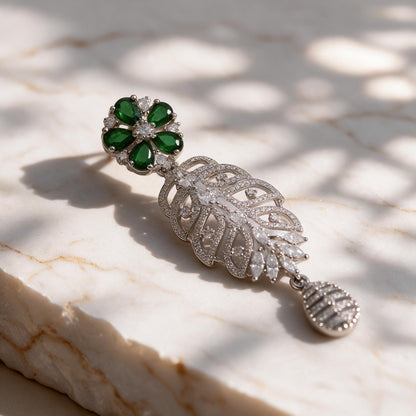 Close-up of a green floral earring top, open leaf-shaped drop and clear-accented teardrop pendant.