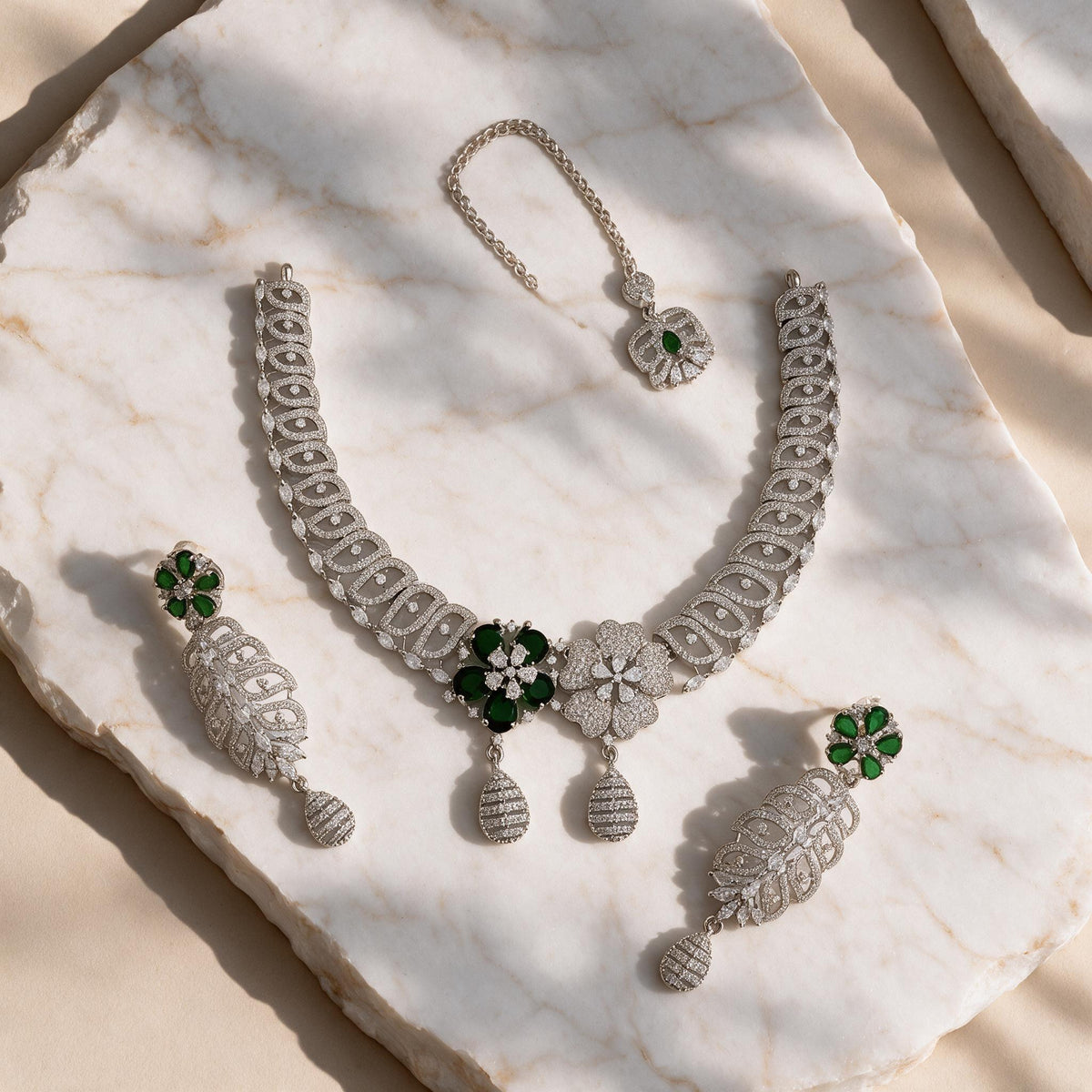 Meher silver-tone necklace, matching green floral drop earrings and chain-mounted floral ornament arranged on marble.