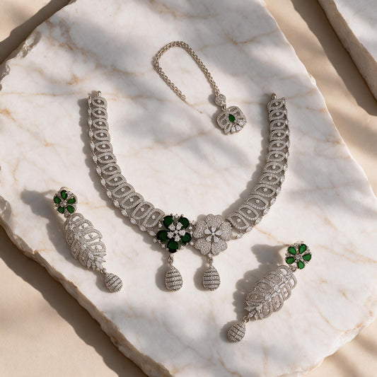 Meher silver-tone necklace, matching green floral drop earrings and chain-mounted floral ornament arranged on marble.
