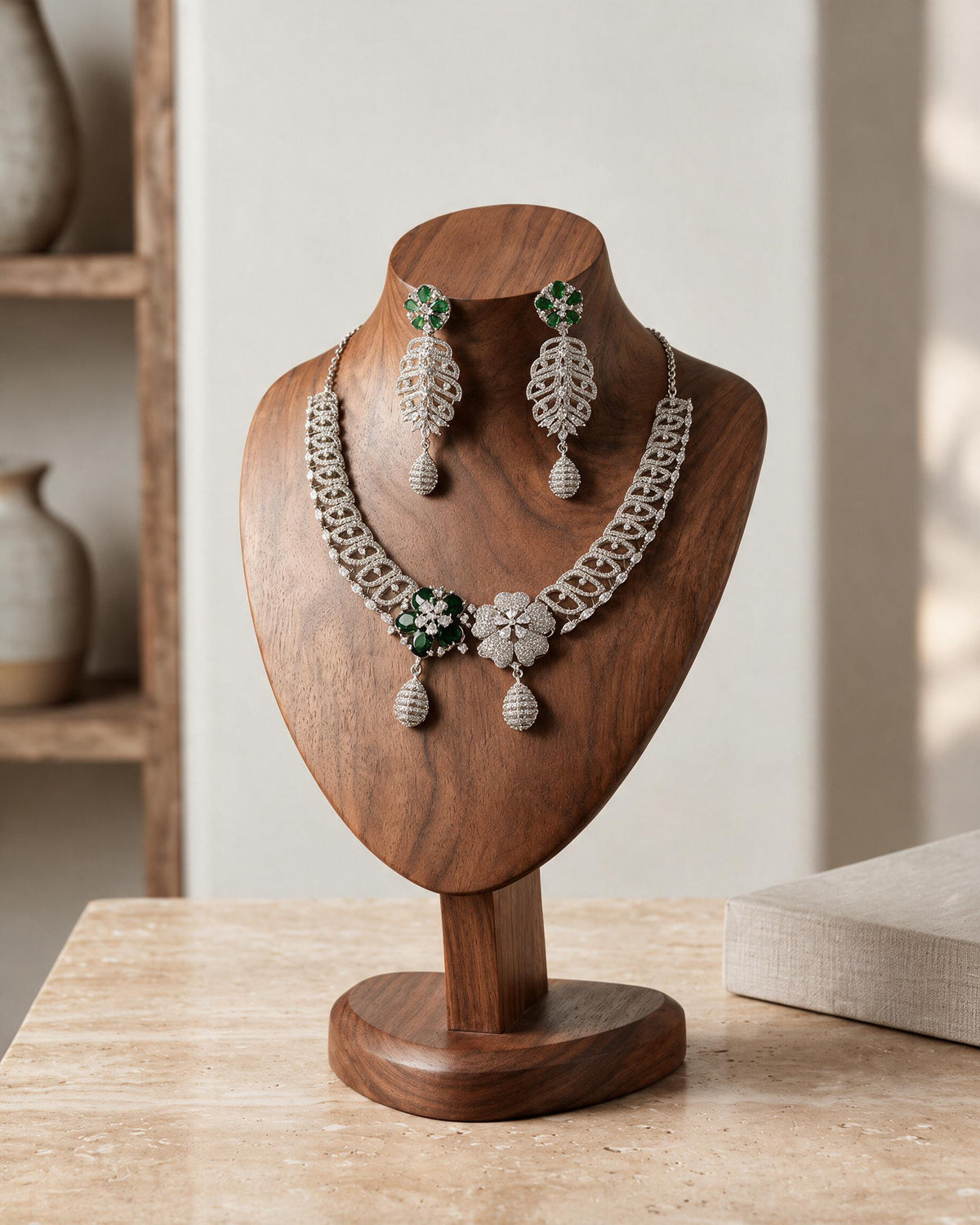 Front view of the Meher necklace and earrings on a wooden display, showing green and clear floral centres.