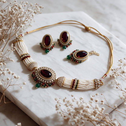 Burgundy and ivory-bead choker with matching earrings and maang tikka on marble.