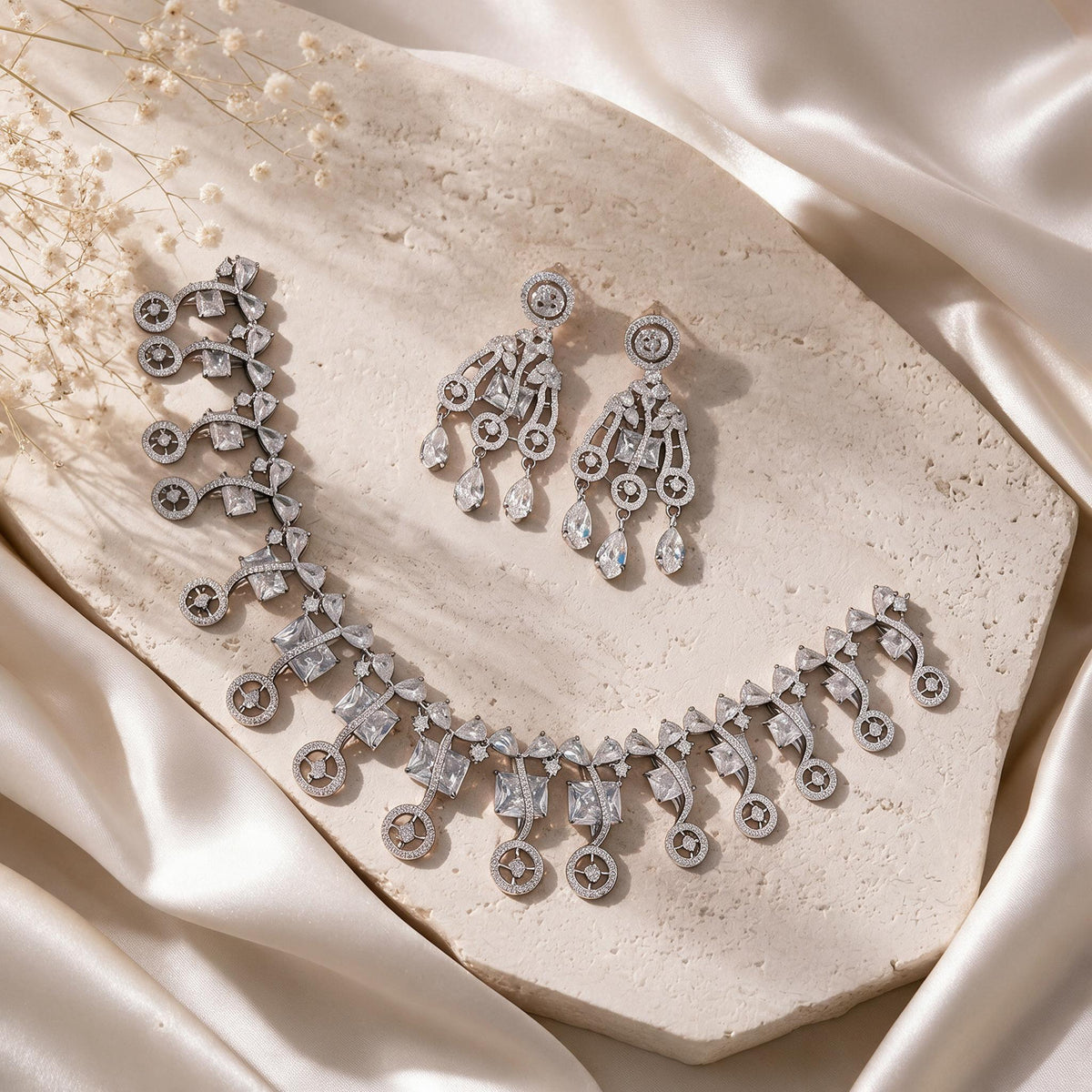 Complete silver-tone necklace and chandelier earrings on a pale stone display.