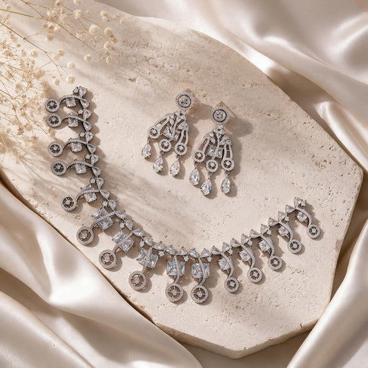 Complete silver-tone necklace and chandelier earrings on a pale stone display.